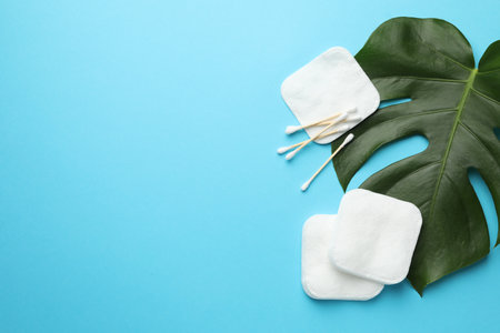 Cotton pads, swabs and monstera leaf on light blue background, flat lay. Space for textの写真素材
