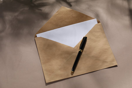 Kraft paper envelope with letter and pen on dark beige background, top view. Mockup for designの写真素材
