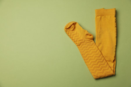 Beautiful yellow child's tights on green background, top view. Space for textの写真素材