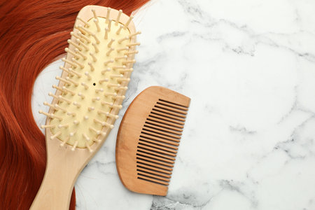 Wooden brush, comb and lock of hair on white marble table, flat lay. Space for textの写真素材