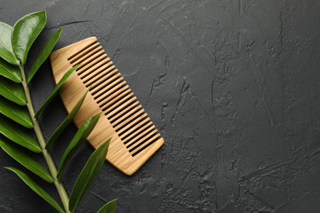 Wooden comb and branch with leaves on dark textured table, flat lay. Space for textの写真素材