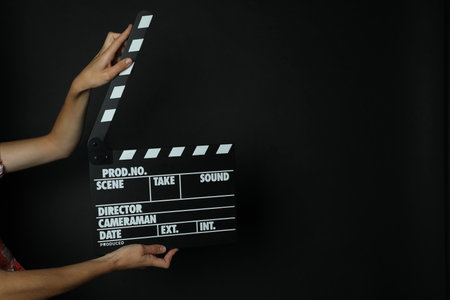 Woman with clapperboard on black background, closeup. Space for textの写真素材