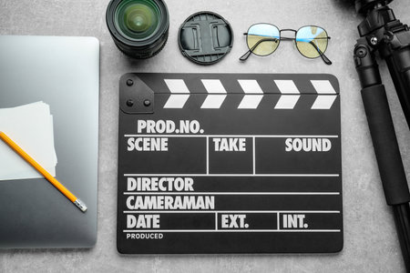 Flat lay composition with movie clapper, camera lens and laptop on gray textured tableの写真素材