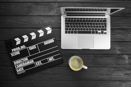 Movie clapper, laptop and cup of coffee on black wooden table, flat layの写真素材