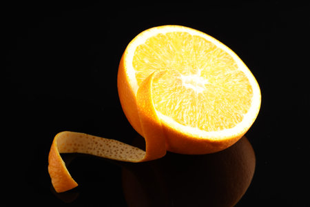 One curly orange peel and half of fruit on black mirror surface, closeupの写真素材