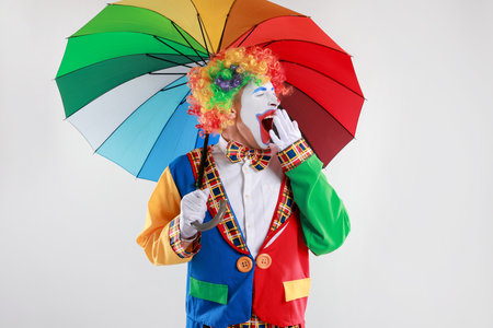 Clown with colorful umbrella yawning on light backgroundの写真素材