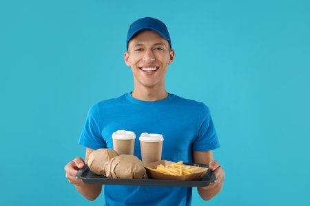 Fast-food worker holding tray with order on light blue backgroundの写真素材