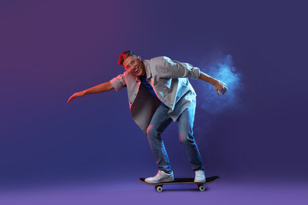 Happy man riding skateboard in color lights against blue backgroundの写真素材