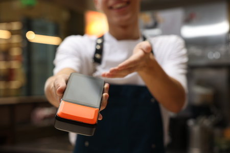 Cafe worker with payment terminal indoors, closeup