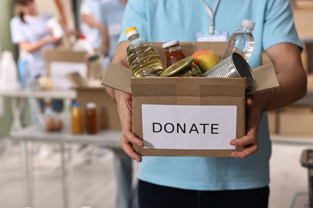 Volunteer holding donation box with food products indoors, closeup. Space for textの写真素材