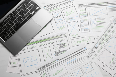 Developing UI design. Sketches of website wireframes and laptop on table, top viewの写真素材