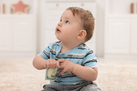 Little baby with dollar banknote on floor at homeの写真素材