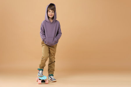 Little boy with skateboard on beige background, space for text