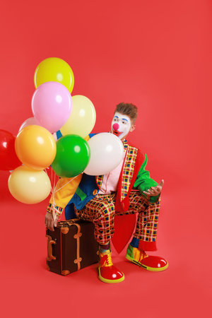 Clown with colorful balloons and suitcase on red backgroundの写真素材