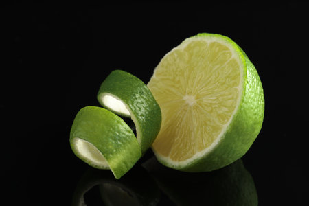 Lime peel and half of fresh fruit on black mirror surface, closeupの写真素材