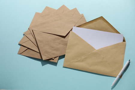 Kraft paper envelopes with letter and pen on light blue background, flat lay. Mockup for designの写真素材