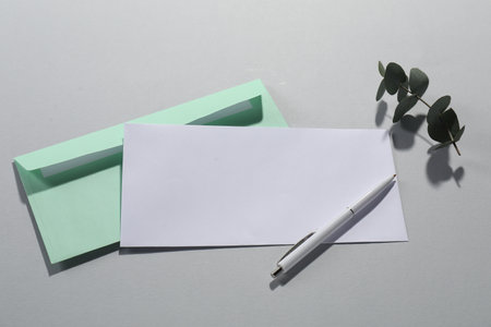 Paper envelopes, pen and eucalyptus branch on gray background, flat lay. Mockup for designの写真素材