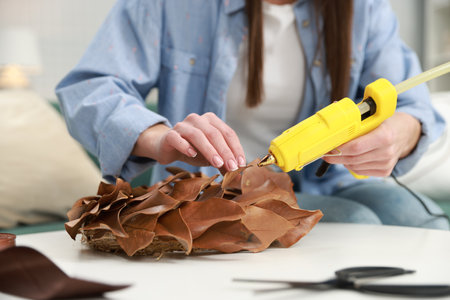 Woman with hot glue gun making craft at table indoors, closeup