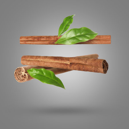 Cinnamon sticks and green leaves in air on grey backgroundの写真素材