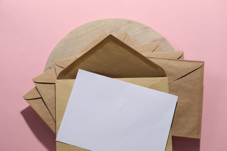 Kraft paper envelopes and letter on pink background, top view. Mockup for design