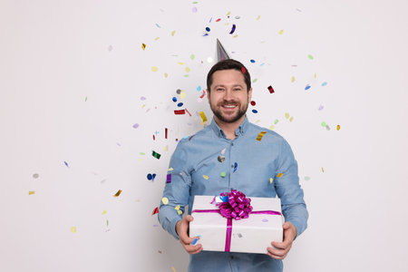 Happy man with gift box under falling confetti on white background. Surprise partyの写真素材