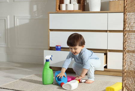 Little boy playing with bottles of detergents near cabinet at home, space for text. Child in dangerの写真素材