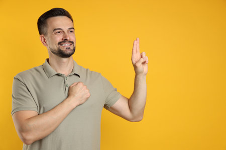 Man showing oath gesture on orange background, space for text. Making a promiseの写真素材