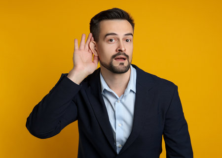 Man showing hand to ear gesture on orange backgroundの写真素材