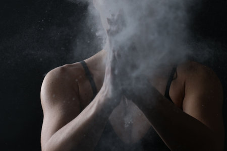 Woman clapping hands with talcum powder before training on black background, closeupの写真素材