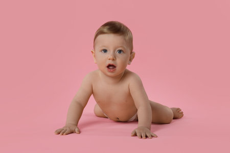 Cute little baby in diaper crawling on pink backgroundの写真素材