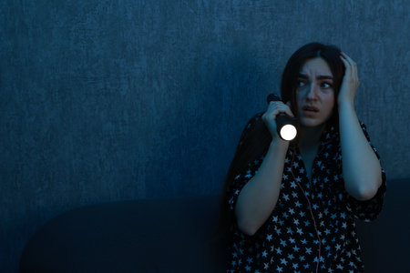 Fear of darkness. Scared young woman with flashlight on couch indoors at night, space for textの写真素材