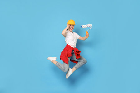 Young decorator with paint roller jumping on light blue backgroundの写真素材