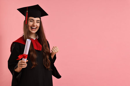 Happy student with diploma after graduation on pink background. Space for textの写真素材