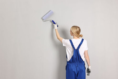 Female worker painting wall with roller indoors, back view. Space for textの写真素材