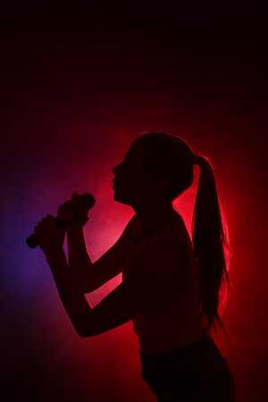 Silhouette of woman singing on dark background with color lightsの写真素材