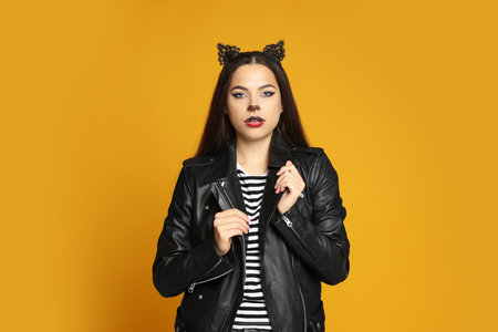 Woman with cat makeup and ears in leather jacket on orange backgroundの写真素材