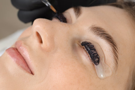 Eyelash lamination procedure. Esthetician applying dye on woman's eyelashes in beauty salon, closeupの写真素材