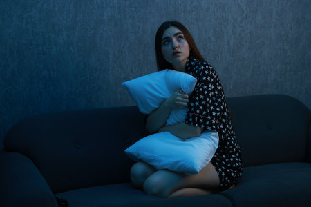 Fear of darkness. Scared young woman hugging pillow on couch indoors at night, space for textの写真素材