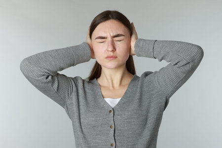 Distressed woman covering her ears from loud noise on light grey backgroundの写真素材