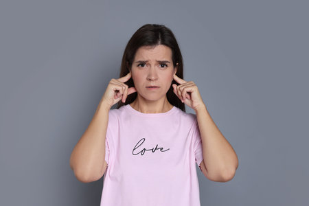 Woman covering her ears with fingers on grey background