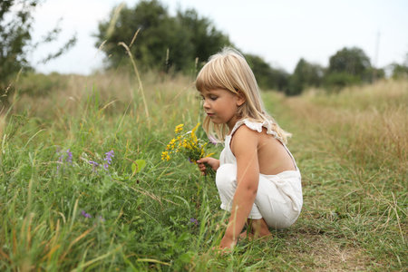 Cute little girl with flowers at meadow. Child enjoying beautiful natureの写真素材