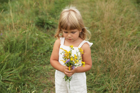 Cute little girl with flowers at meadow. Child enjoying beautiful natureの写真素材