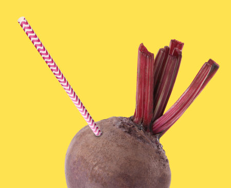 Drinking straw sticking out of fresh beetroot on yellow background. Freshly made juice or smoothie conceptの写真素材