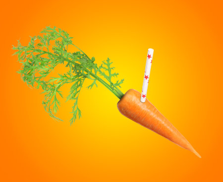 Drinking straw sticking out of fresh carrot on orange background. Freshly made juice or smoothie conceptの写真素材