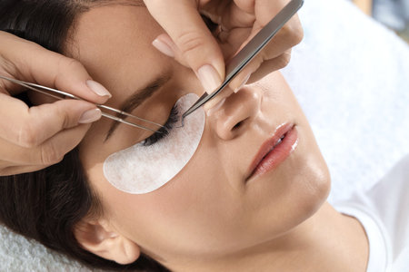 Woman undergoing lash extensions procedure in beauty salon, closeup
