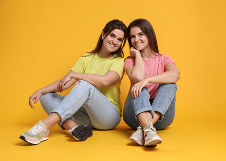 Portrait of happy twin sisters on orange backgroundの写真素材