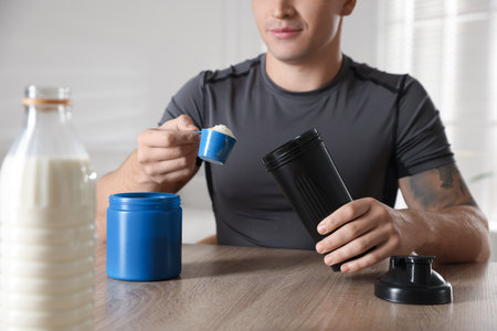 Making protein cocktail. Man with scoop of powder and shaker at wooden table, closeupの写真素材