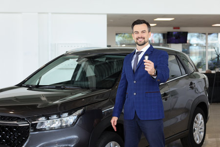 Happy salesman holding key near new black car in salonの写真素材