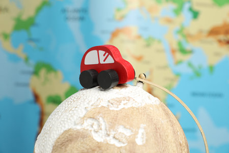 Red toy car on globe against world map, closeup. Road tripの写真素材