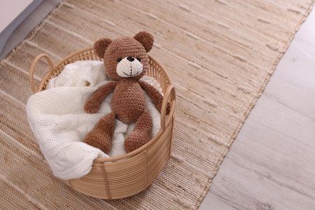 Wicker basket with blanket and toy bear on floor indoors. Space for textの写真素材